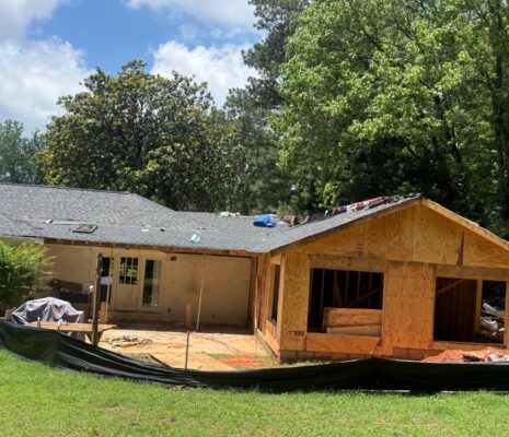 House under renovation with a new wooden extension being built on the right, exposed framing and construction debris in the yard.